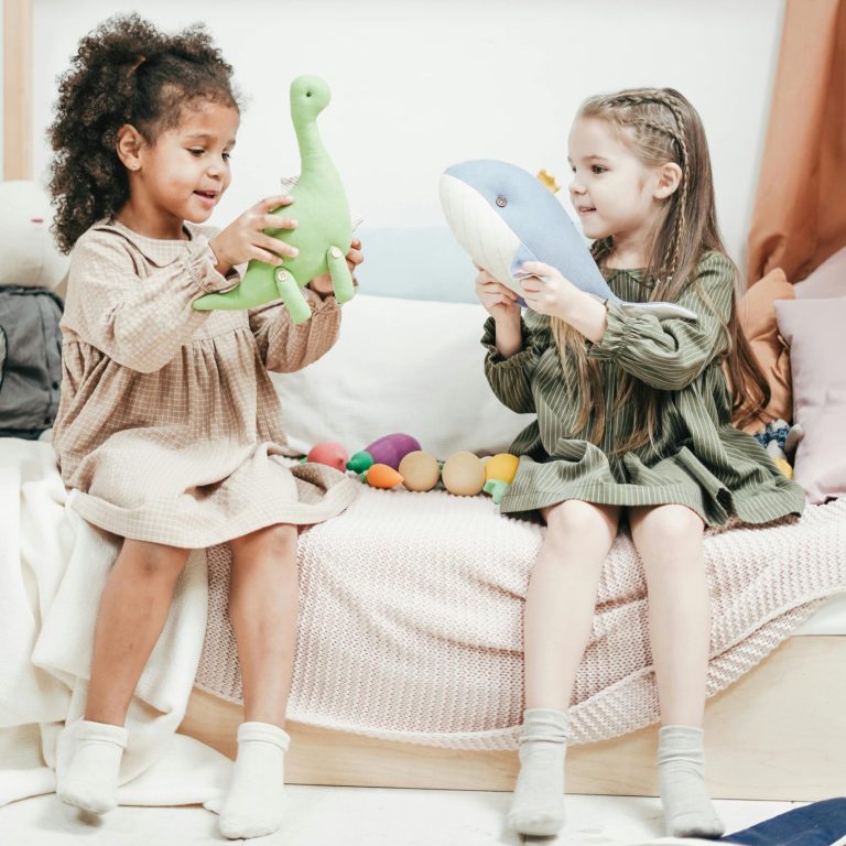 play therapy in frisco, tx. two young girls playing with dinosaur dolls sitting on the side of the bed.